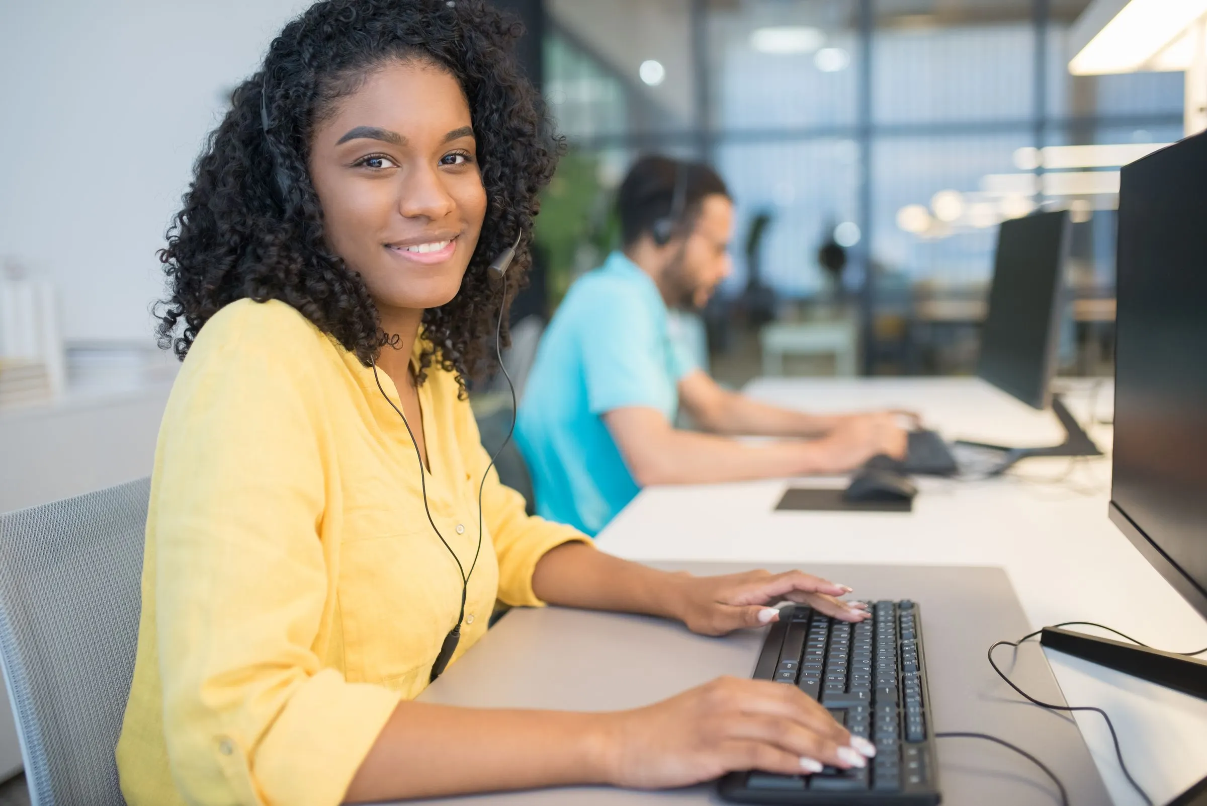 A smiling contact-centre agent wearing a headset at her desk