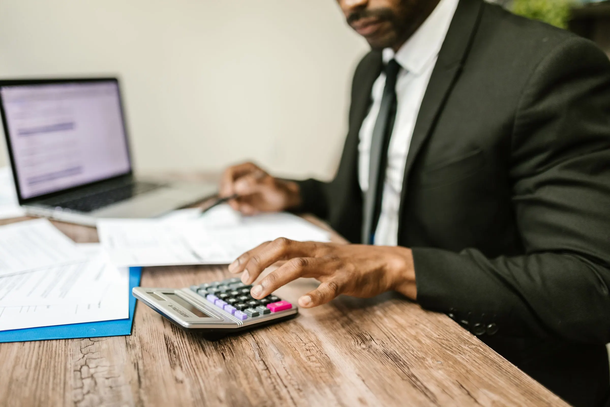 A finance professional working with a calculator beside a laptop