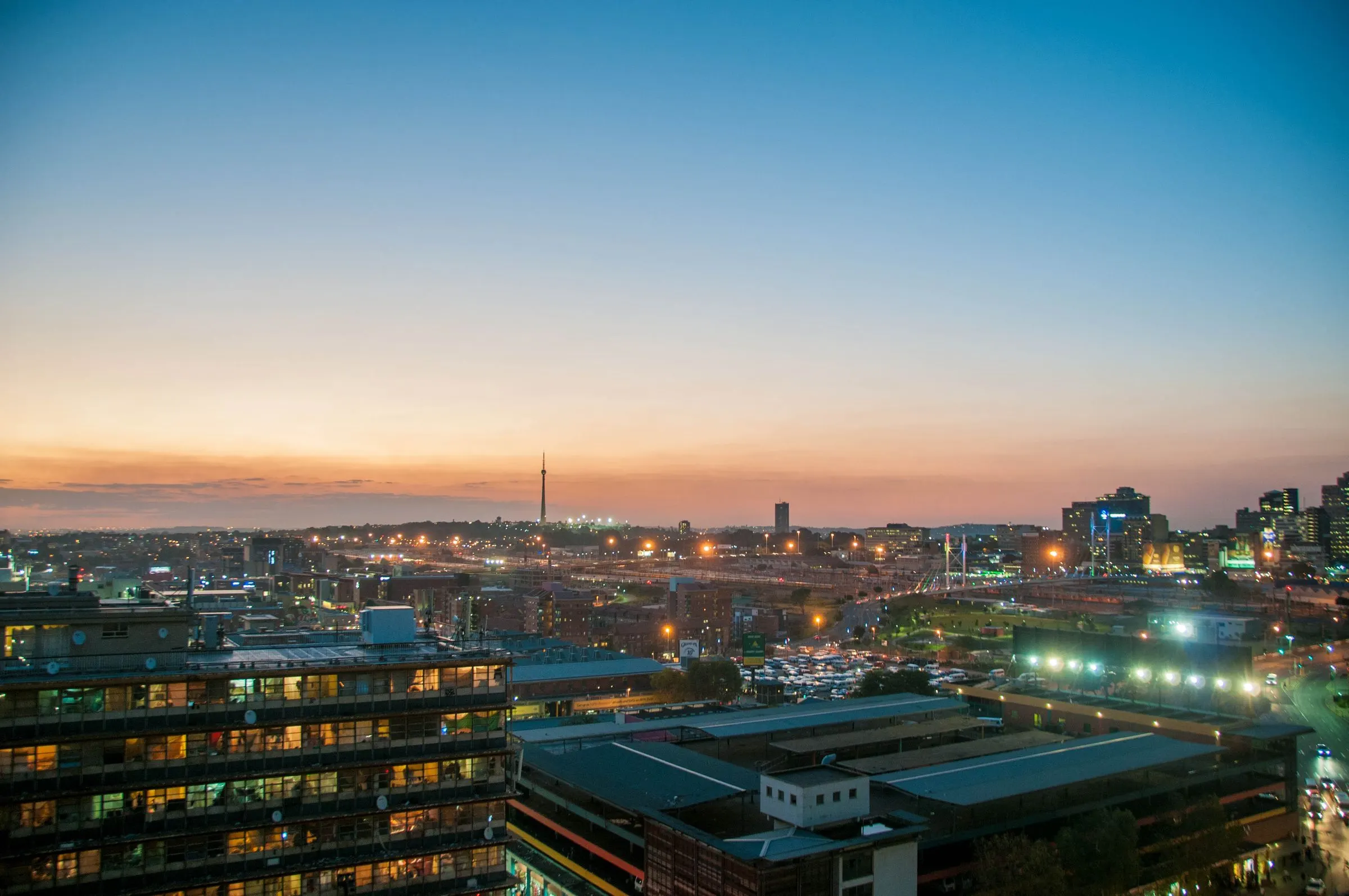 Johannesburg at dusk, with city lights below an orange and blue sky and the Hillbrow tower on the horizon